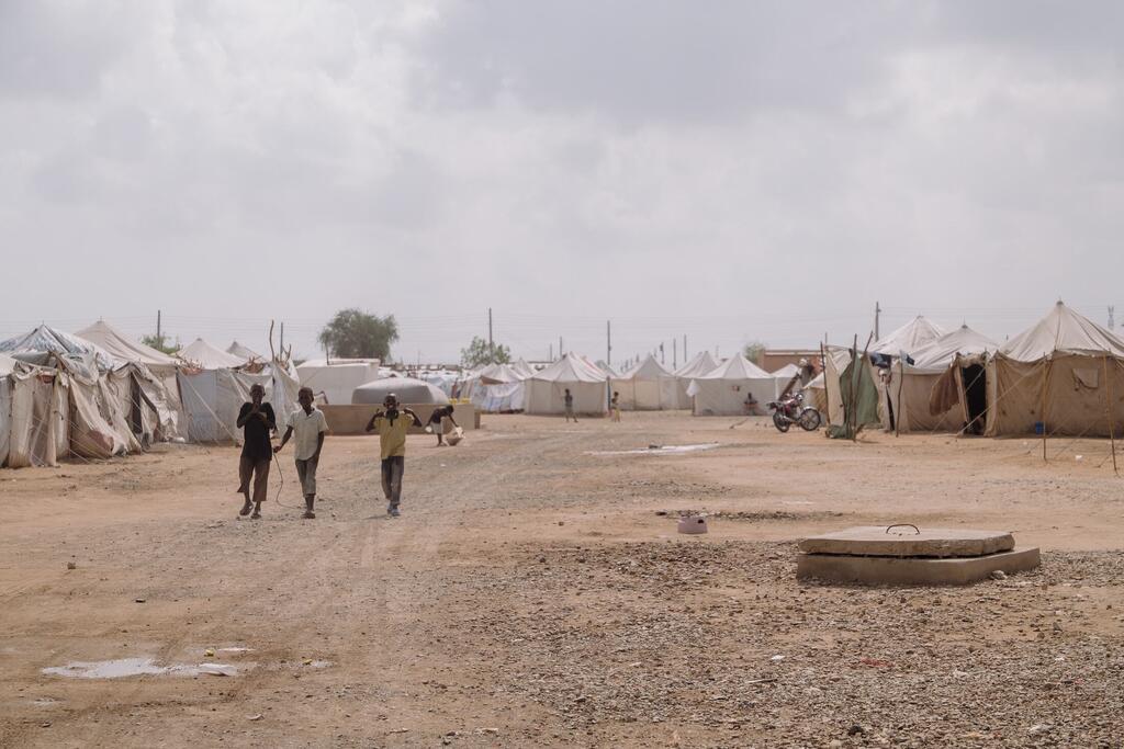 Les enfants marchent entre des rangées de tentes d'urgence à As-Senniya IDP site à Port-Soudan, au Soudan, où les familles déplacées ont cherché refuge contre la violence.
