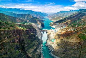 Vista aérea de una enorme presa hidroeléctrica incrustada en un profundo cañón de montaña con agua turquesa que fluye a través, mostrando la infraestructura de energía limpia.