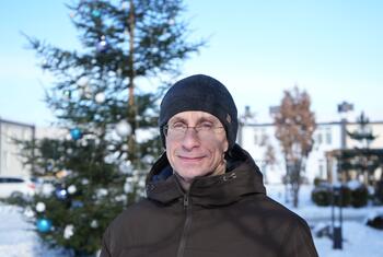 Yurii Shapovalov, a doctor from Ukraine, stands outdoors in winter near a decorated Christmas tree, smiling after being released from nearly eight years of captivity during the war.