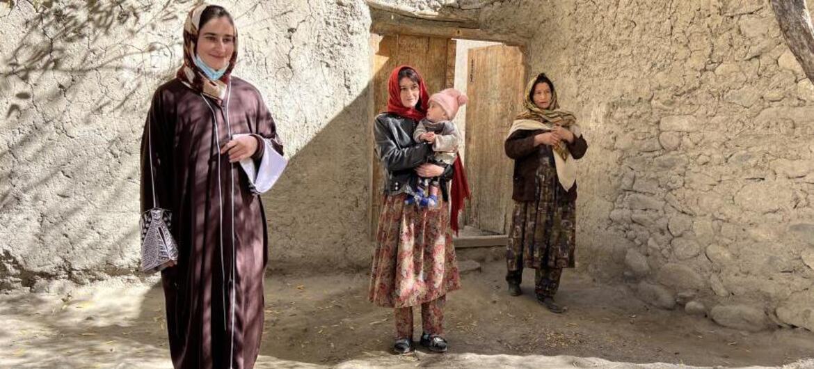 Trois femmes afghanes, dont des mères qui tiennent des bébés, se tiennent devant une maison traditionnelle en briques de boue dans un cadre rural, soulignant les efforts d'aide humanitaire du Programme alimentaire mondial.