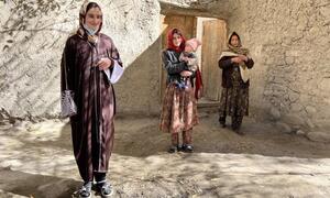 Trois femmes afghanes, dont des mères qui tiennent des bébés, se tiennent devant une maison traditionnelle en briques de boue dans un cadre rural, soulignant les efforts d'aide humanitaire du Programme alimentaire mondial.