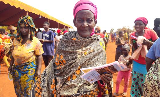 A woman holding a document in a refugee camp in Tanzania, surrounded by other displaced persons, highlighting the situation of Burundian refugees and voluntary repatriation efforts.