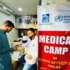 पंजाब, पाकिस्तान में बाढ़ प्रभावित समुदायों को स्वास्थ्य सेवाएं प्रदान करने वाला डब्ल्यूएचओ का एक मोबाइल चिकित्सा शिविर, जिसमें एक स्वास्थ्य कार्यकर्ता एक रोगी की सहायता कर रहा है।