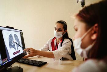 Une femme médecin portant un masque montre une radiographie thoracique des poumons sur un moniteur d'ordinateur alors qu'elle parle à un patient aussi masqué.