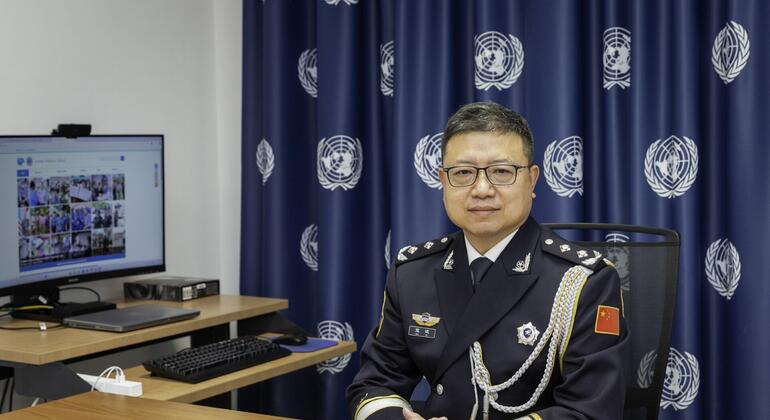 一个穿着中国军装的男子坐在办公室的办公桌上,背景是联合国旗.
