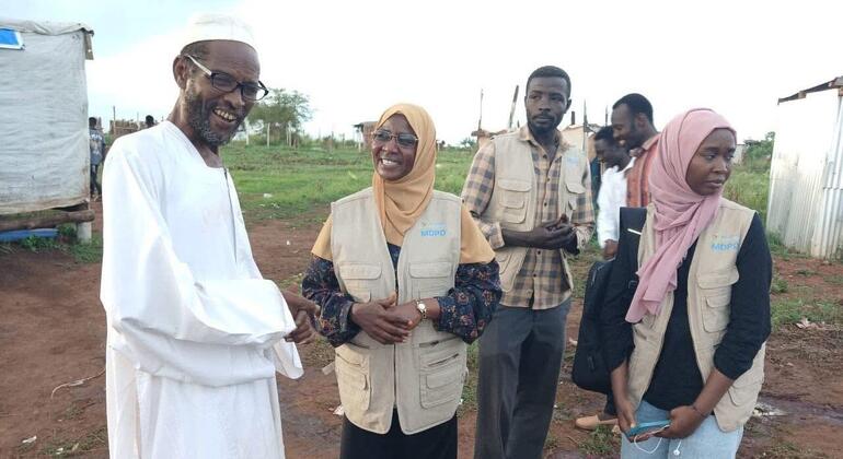 رجل أفريقي يرتدي عباءة بيضاء وقبعة يصافح اثنتين من عاملات الإغاثة اللاتي يرتدين سترات وحجابات MDPD في بيئة ريفية في الهواء الطلق.