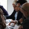 Um grupo diversificado de profissionais vestidos de negócios reúne-se em torno de uma mesa numa sala de reuniões, revisando documentos e discutindo estratégias.
