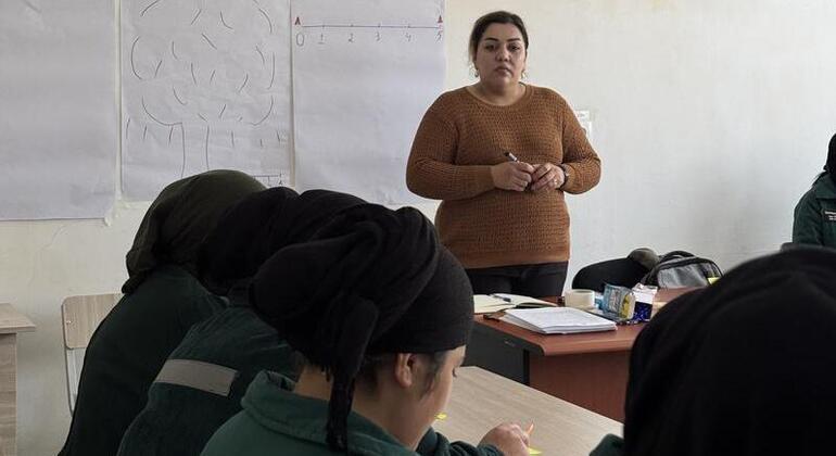 В Таджикистане женщина-инструктор стоит перед классом и преподает группе учеников, которые сидят за столами.