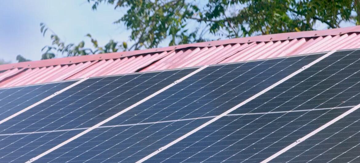 Panneaux solaires installés sur un toit en métal ondulé rose avec des arbres et du ciel en arrière-plan.