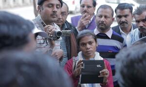 Una joven reportera india sostiene una tableta, rodeada de un grupo de hombres, destacando el papel de las mujeres en el cambio de las narrativas de los medios de comunicación en la India.