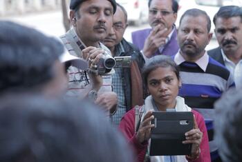 Una joven reportera india sostiene una tableta, rodeada de un grupo de hombres, destacando el papel de las mujeres en el cambio de las narrativas de los medios de comunicación en la India.