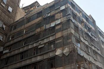 A multi-story concrete building in Iran with a weathered facade, featuring numerous windows and some scaffolding.