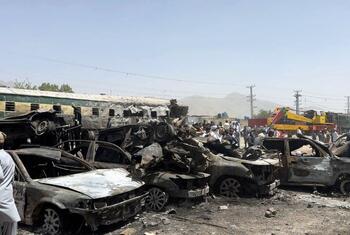 Wreckage from a train and car attack in Quetta, Pakistan, with damaged vehicles and a crowd of people at the scene.