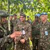 Um grupo de soldados da ONU com uniformes camuflados e boinas azuis ouve um briefing em uma floresta.