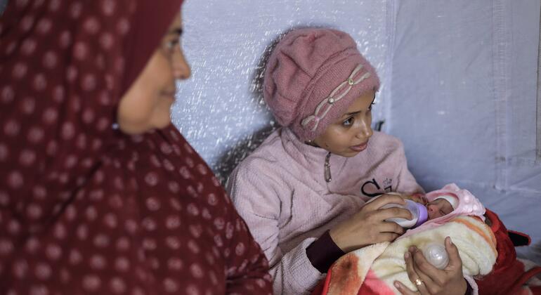Una mujer, identificada como Rana, sostiene a su bebé mientras su suegra se sienta a su lado en una tienda de campaña.