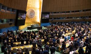 A large crowd stands in solemn silence at the United Nations General Assembly hall during a Holocaust commemoration event, honoring victims with prayers and a moment of reflection.