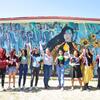 A group of student artists proudly standing in front of the 'Warrior Woman' mural they created, celebrating their work in Mexico.
