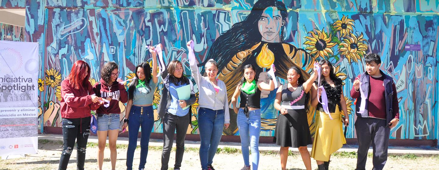 A group of student artists proudly standing in front of the 'Warrior Woman' mural they created, celebrating their work in Mexico.