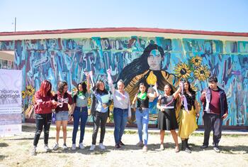 A group of student artists proudly standing in front of the 'Warrior Woman' mural they created, celebrating their work in Mexico.