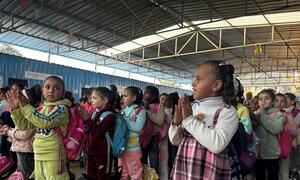 Un grupo de niños palestinos están de pie en un centro de aprendizaje temporal en Gaza, aplaudiendo.