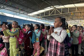Un grupo de niños palestinos están de pie en un centro de aprendizaje temporal en Gaza, aplaudiendo.