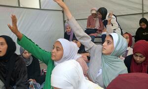 Los niños levantan las manos para responder preguntas en un centro de aprendizaje apoyado por UNICEF en la Escuela Aeshyia en Deir al-Balah, Gaza, estudiando bajo tiendas de campaña en medio de infraestructuras dañadas.