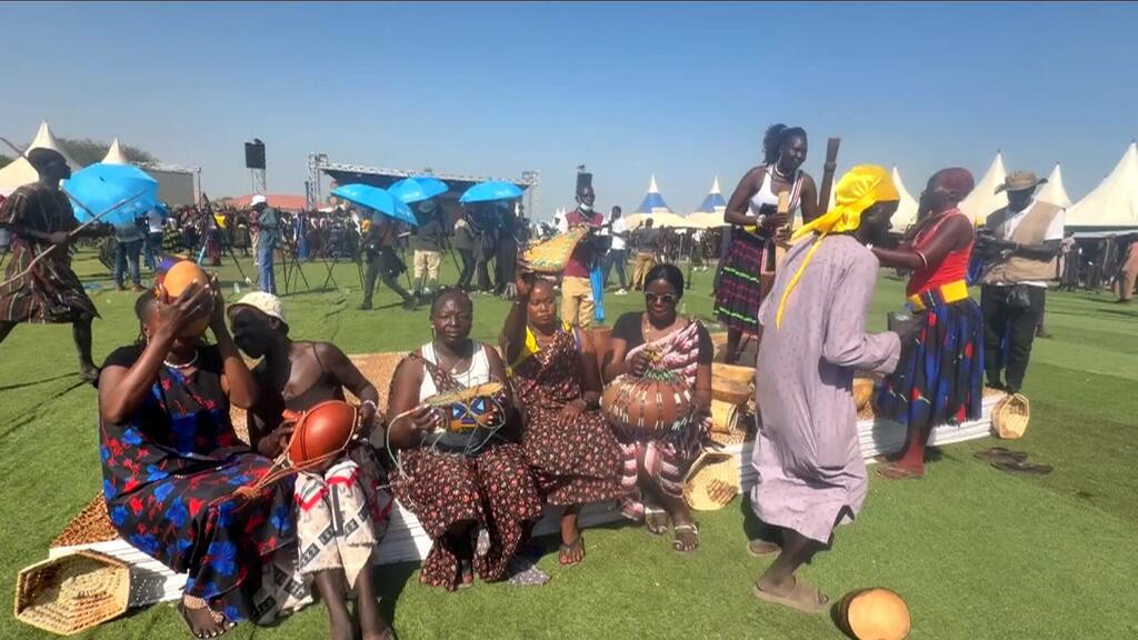 Kikundi cha watu kwenye tamasha la ndani huko Sudan Kusini, wakionyesha ufundi wa jadi na kukuza amani na biashara chini ya bendera ya UNMISS.