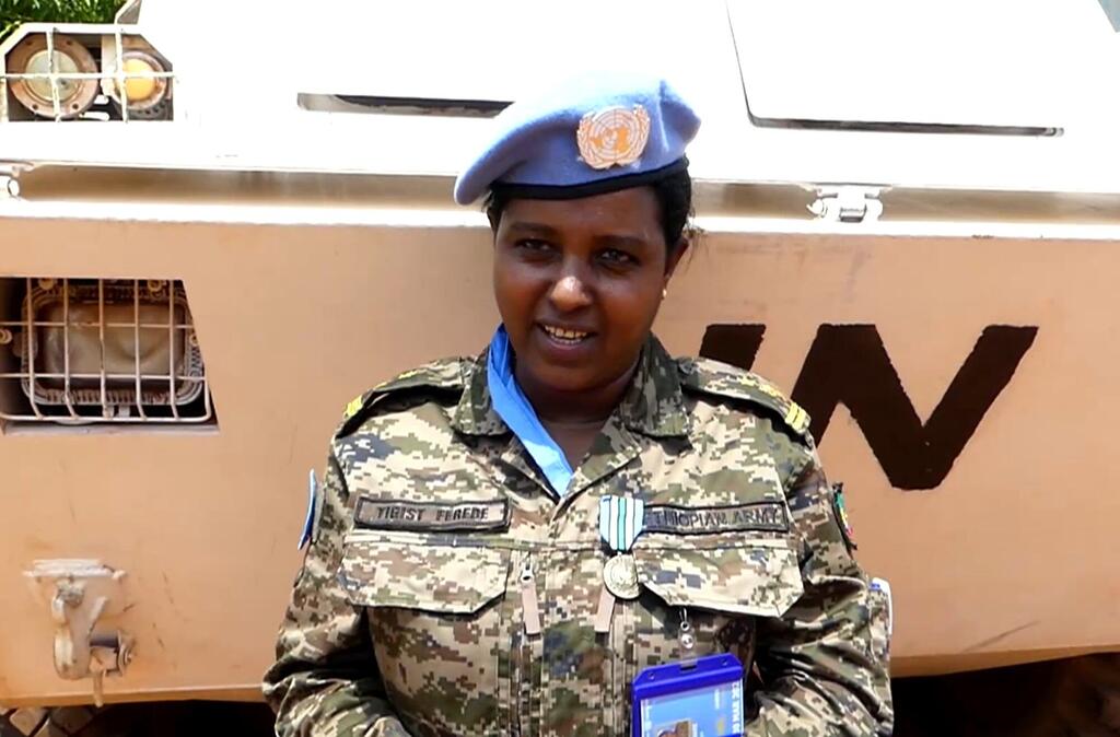 Mwanamke ambaye ni fundi wa mitambo wa jeshi la Ethiopia, Tigist Felede, akivaa sare ya kijeshi akiwa na beret ya wanajeshi wa kulinda amani wa Umoja wa Mataifa, akiwa amesimama mbele ya gari la kijeshi.