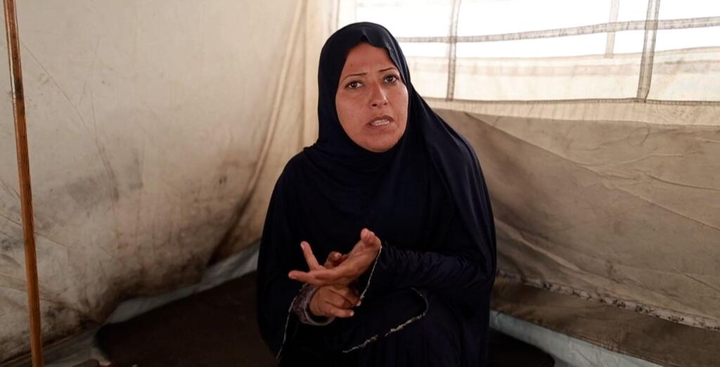 امرأة فلسطينية ترتدي حجابًا أسود تجلس داخل خيمة في غزة، تتحرك بأيديها بينما تتحدث.