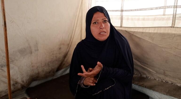 امرأة فلسطينية ترتدي حجابًا أسود تجلس داخل خيمة في غزة، تتحرك بأيديها بينما تتحدث.