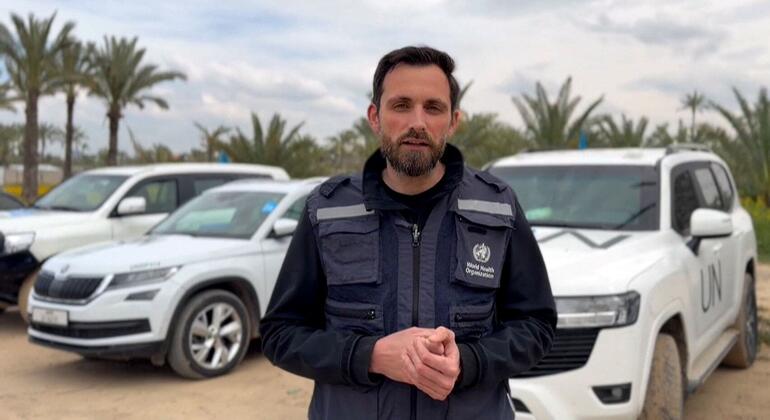 رجل يرتدي سترة منظمة الصحة العالمية يقف أمام مركبات الأمم المتحدة في غزة.