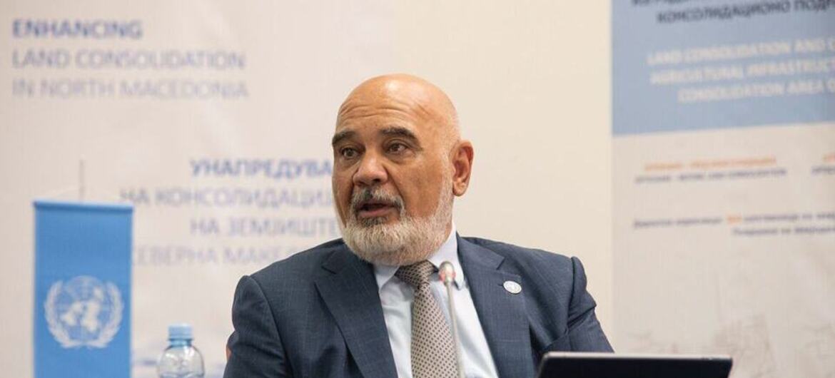 Мужчина из Ближнего Востока с лысой головой и серой бородой, в костюме и галстуке, говорит в микрофон на конференции. Флаг ООН виден на столе перед ним.