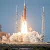 The NASA SLS rocket with the Orion spacecraft on top launches from Kennedy Space Center in Florida, marking the beginning of the Artemis II mission. The massive rocket ascends into the sky, leaving a trail of bright exhaust and billowing smoke.