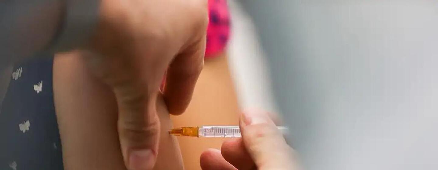 Uma imagem em close-up de um profissional de saúde administrando uma injeção da vacina contra o HPV no braço de uma criança no Brasil.