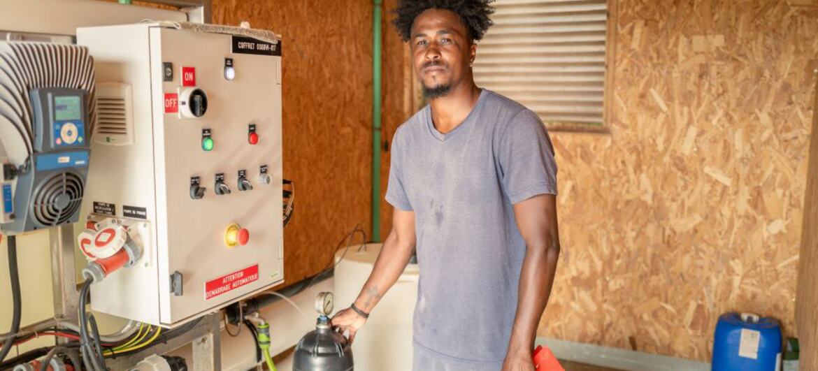 Um homem está ao lado de um equipamento de irrigação em um ambiente rural em Cabo Verde, simbolizando o retorno dos migrantes para construir um futuro em suas comunidades através da agricultura.
