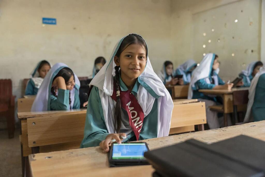 پاکستان میں ایک نوجوان لڑکی کلاس روم میں ٹیبلٹ استعمال کرتے ہوئے مسکرا رہی ہے۔ یہ سندھ لرننگ پاسپورٹ پروگرام کا حصہ ہے جو لڑکیوں کو ڈیجیٹل تعلیم کے ذریعے بااختیار بناتا ہے۔