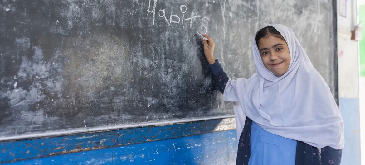 بلوچستان، پاکستان میں ایک کلاس روم میں ایک سفید حجاب اور نیلے رنگ کی وردی میں ایک نوجوان لڑکی نے یونیسف اور گلوبل پارٹنرشپ فار ایجوکیشن کی مدد سے ایک بورڈ پر 'اچھی عادتیں' لکھیں۔