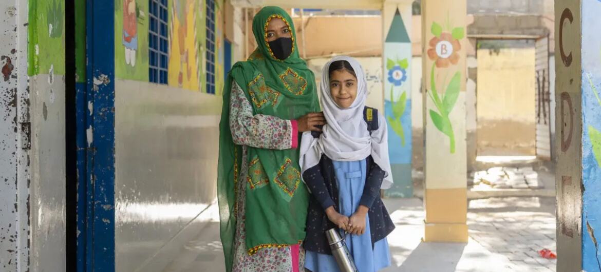 ایک استاد اور ایک نوجوان طالبہ بلوچستان، پاکستان میں ایک رنگارنگ اسکول کوریڈور میں اکٹھے کھڑے ہیں، جو یونیسیف اور جی پی ای کی حمایت سے تعلیمی تبدیلی کی علامت ہے۔