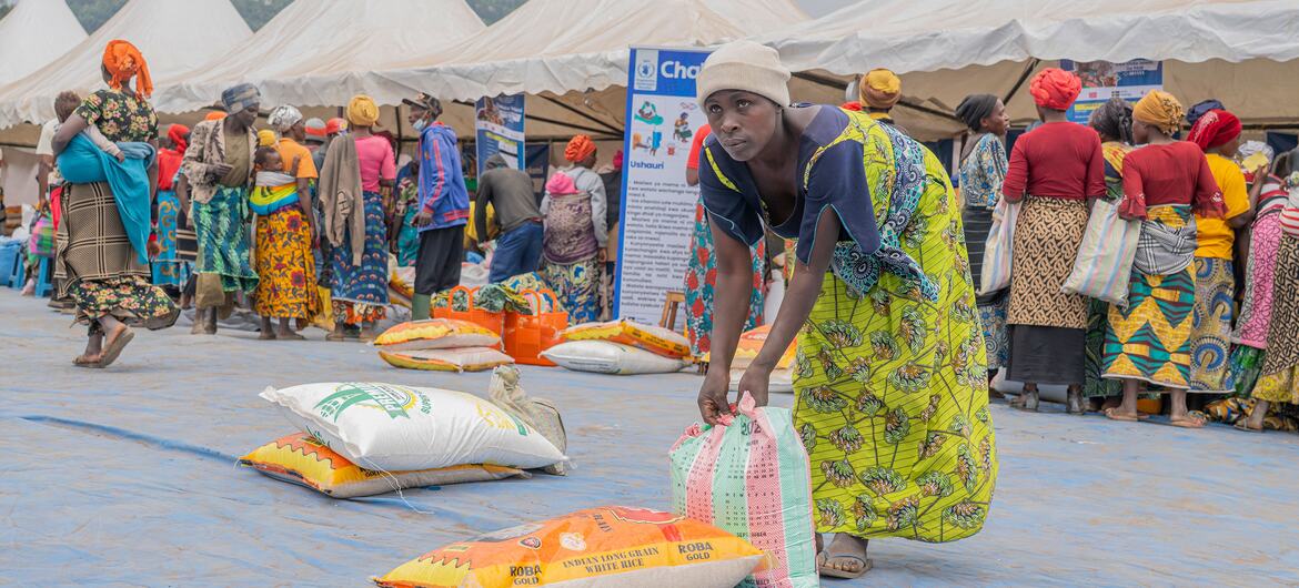 A woman in a vibrant green dress picks up a bag of rice at a local market in DR Congo, part of the World Food Programme's Chakula Sokoni food assistance initiative. The project provides electronic vouchers to displaced families, enabling them to purchase food from local traders and improve household nutrition.