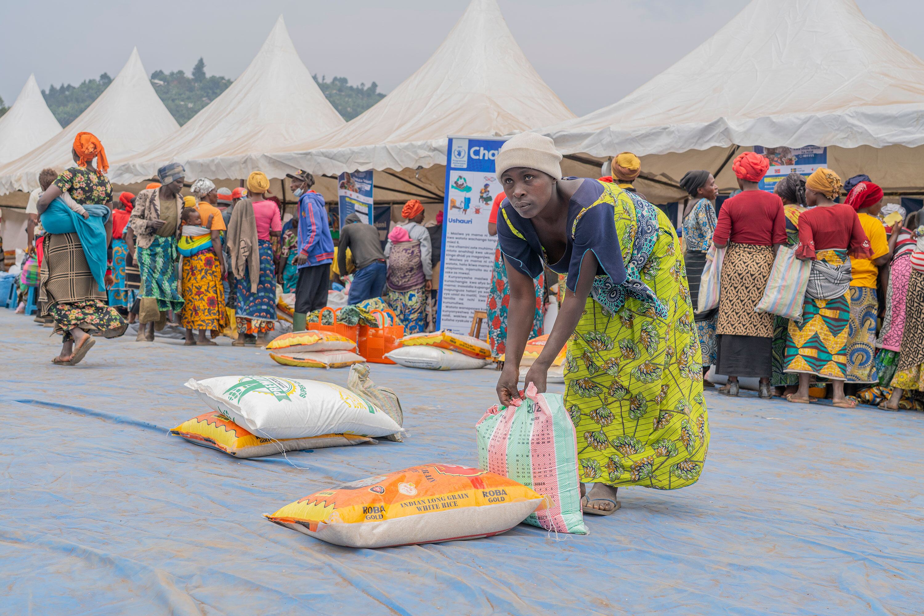 Une femme vêtue d'une robe verte vibrante récupère un sac de riz sur un marché local de la RDC, dans le cadre de l'initiative d'aide alimentaire Chakula Sokoni du Programme alimentaire mondial.