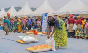 A woman in a vibrant green dress picks up a bag of rice at a local market in DR Congo, part of the World Food Programme's Chakula Sokoni food assistance initiative. The project provides electronic vouchers to displaced families, enabling them to purchase food from local traders and improve household nutrition.