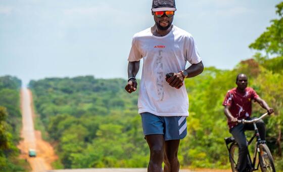 Mwanariadha aitwaye Deo Kato anakimbia barabarani nchini Afrika Kusini, akiwa na mtu mwingine kwenye baiskeli.