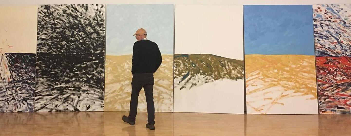 Sandy Walker, an American painter and printmaker, stands in a gallery looking at a series of his large-scale abstract paintings.
