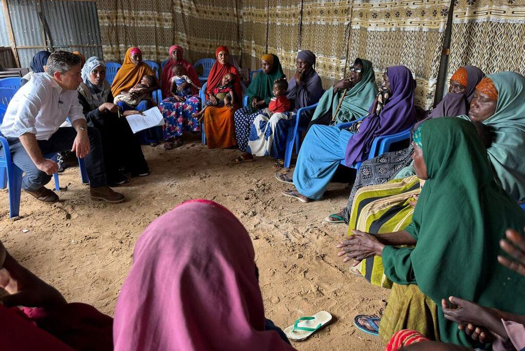 Tom Fletcher anaketi pamoja na kikundi cha wanawake na watoto waliohamishwa katika Kituo cha Lishe cha Youthlinksomal nje ya Mogadishu, Somalia, wakijadili athari za kupunguza fedha kwa maisha yao wakati wa vurugu na mashambulizi ya drone.