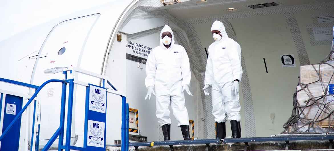 Two health workers in white hazmat suits stand at the open cargo door of an airplane at Bunia airport in DR Congo, during an Ebola emergency response supply delivery.