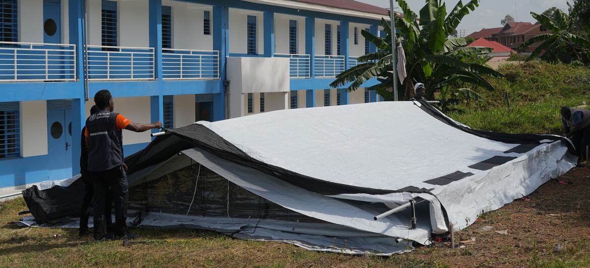 WHO workers set up a temporary tent structure next to a blue and white building in the Democratic Republic of the Congo as part of the response to an Ebola outbreak.
