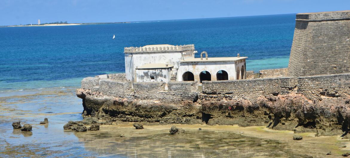 Forte histórico de pedra numa costa rochosa em Moçambique, com o oceano e um céu azul claro ao fundo.