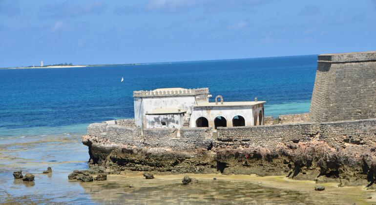 Forte histórico de pedra numa costa rochosa em Moçambique, com o oceano e um céu azul claro ao fundo.