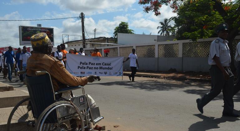 Uma pessoa em cadeira de rodas segura um cartaz que diz "Pela Paz em Casa! Pela Paz no Mundo!" durante uma manifestação pública em Moçambique.