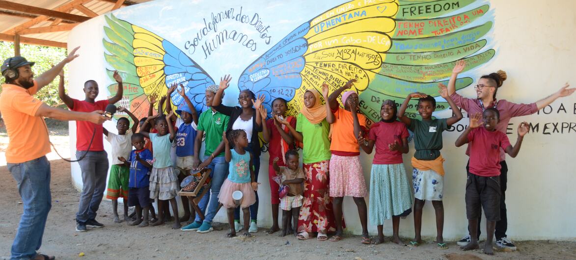 Um grupo de adultos e crianças posa diante de um mural colorido com as palavras "FREEDOM" e "Direitos Humanos" em Moçambique.